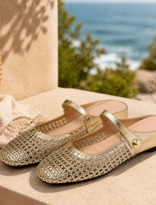 Maisie mule flats in Gold — pair on a sandstone step by the coast