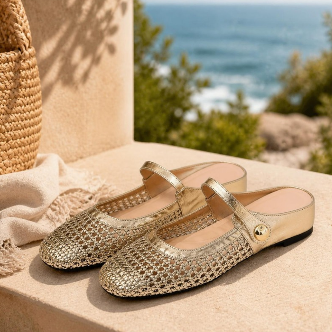 Maisie mule flats in Gold — pair on a sandstone step by the coast