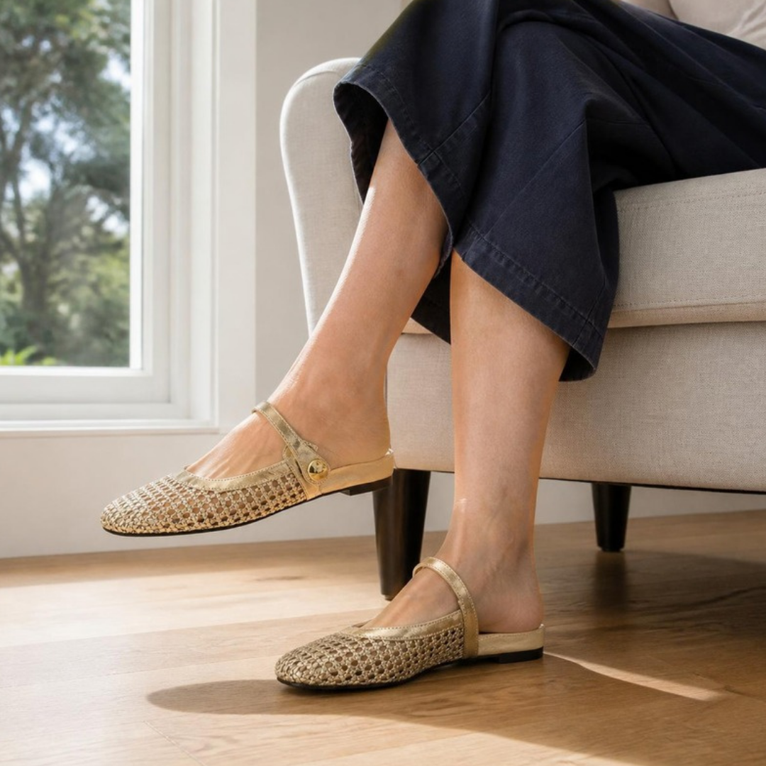 Maisie mule flats in Gold — worn seated in an armchair with legs crossed and a denim midi skirt